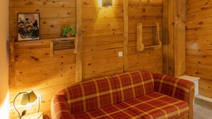 Ein Holzblockhaus-Interieur mit einem Karomuster-Sofa, einem Wandregal mit einem Bild und einer Wandleuchte.