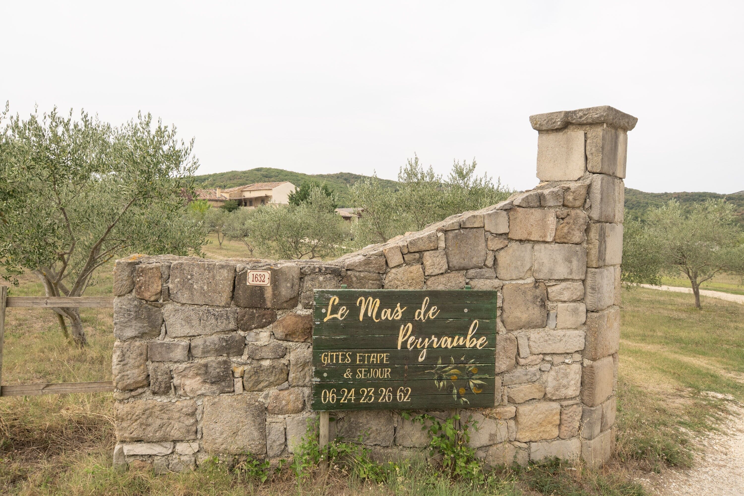 Un mur de pierres sur lequel est apposée une plaque indiquant « Le Mas de Peyraube » et les dates « 06-24 23 26 62 ».