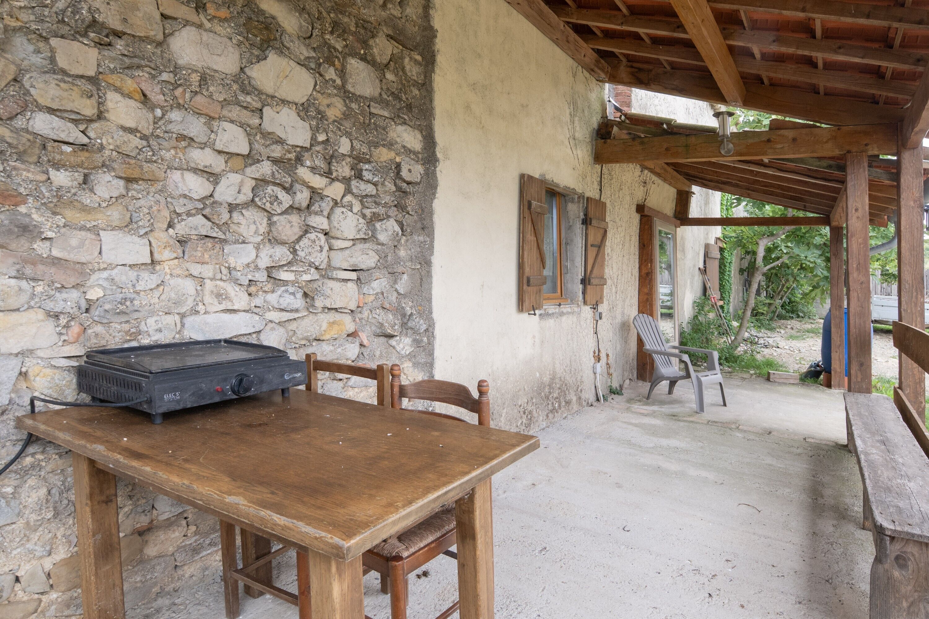 Un espace de restauration extérieur de style rustique, avec un mur en pierre, une table en bois et des chaises.