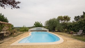 Ein rechteckiger Swimmingpool mit weißer Liegefläche, umgeben von Kies und Grünpflanzen.