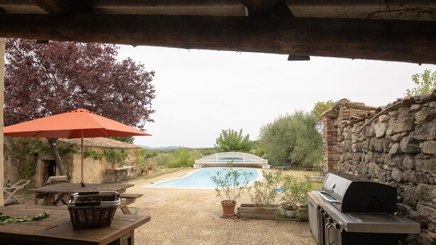 Eine Terrasse mit Grill, Tisch mit Korb, Sonnenschirm und Swimmingpool.