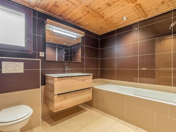 A modern bathroom with a wooden ceiling, a large mirror, a sink with a wooden cabinet, a bathtub, and a toilet.