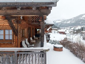 A wooden chalet with a balcony, chairs, and a hot tub.