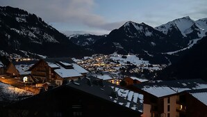 Un village de montagne enneigé, baigné par la lumière du crépuscule, avec des bâtiments illuminés et une vue dégagée sur les sommets environnants.