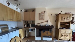 Une cuisine compacte avec des meubles en bois, un four à micro-ondes, un évier et une table à manger recouverte d’une nappe à motifs en forme de cœur.