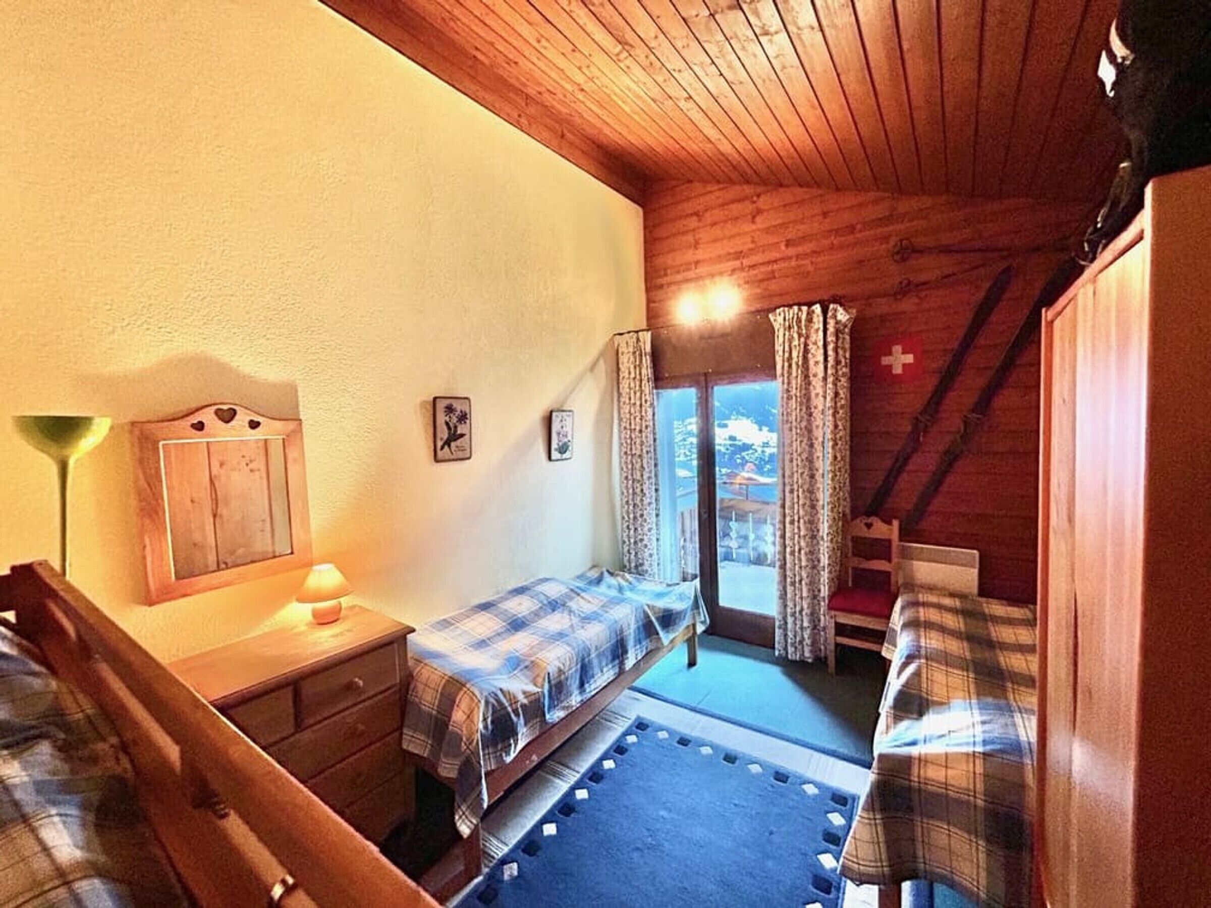 Et hyggeligt værelse med to senge, træloft og et vindue med gardiner.
