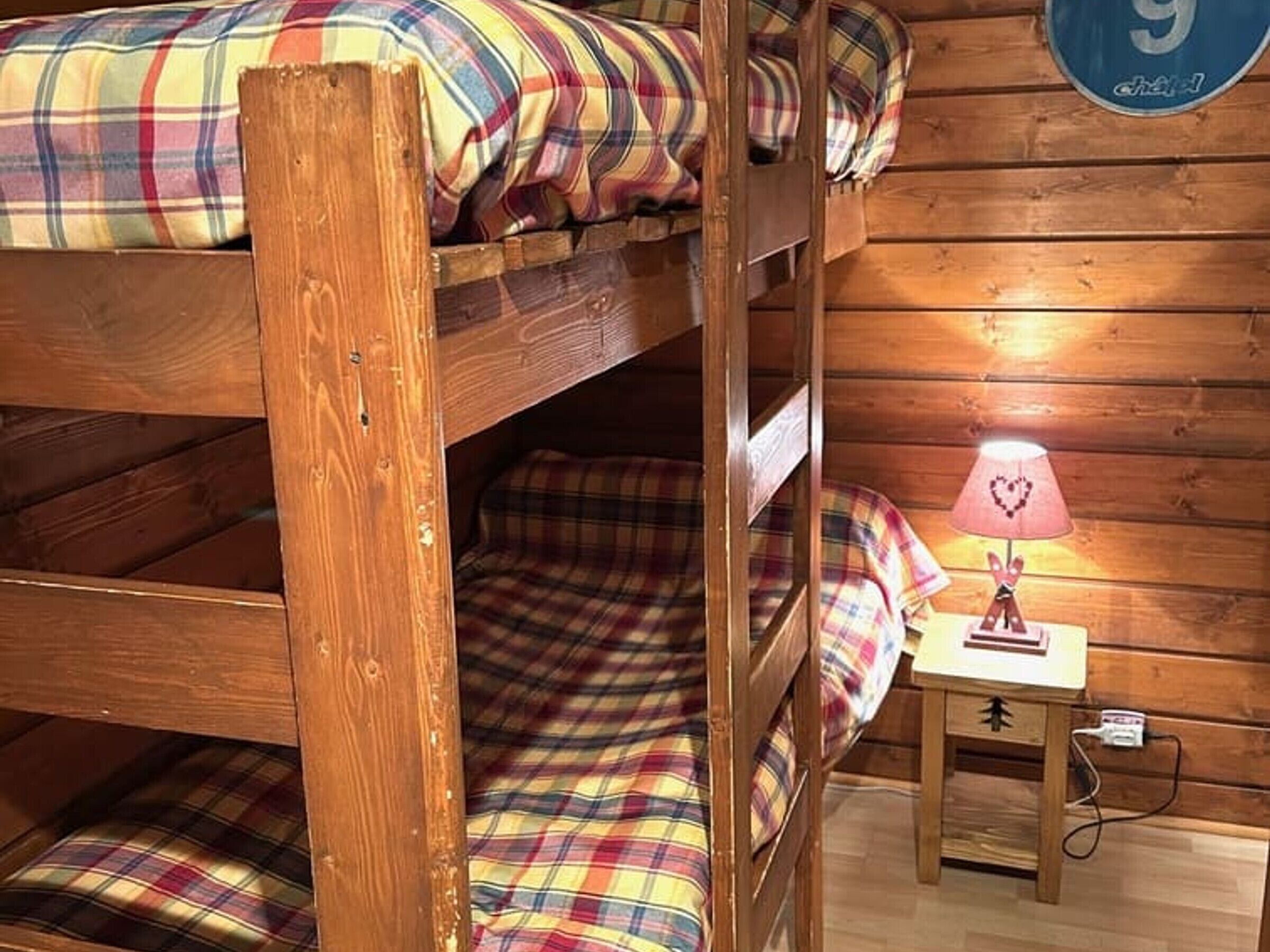 Una cama litera con ropa de cama escocesa, una mesita de noche pequeña con una lámpara, y una pared de madera con el número 9.