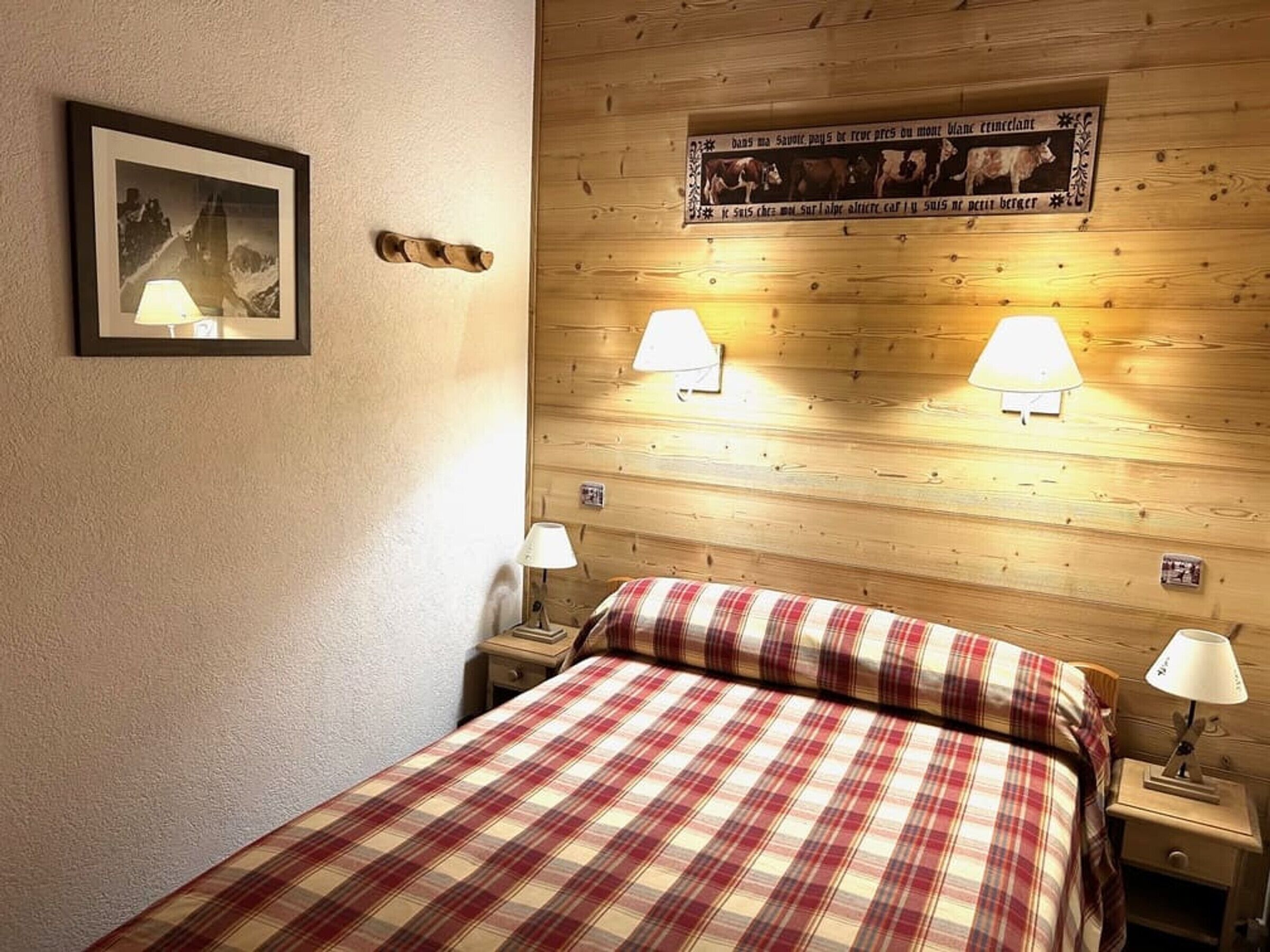Une chambre à coucher avec une tête de lit en bois, deux lampes de chevet, une couverture à carreaux et un tableau encadré au mur.