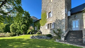 A stone building with a well-maintained lawn, a staircase leading to the entrance, and a mountain in the background. - Guest Room – Château de la Rive – Sleeps 10 (Cruet)