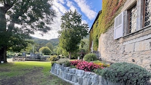 A stone building with a stone wall and a garden with flowers and shrubs. - Guest Room – Château de la Rive – Sleeps 10 (Cruet)