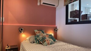 A bedroom with a bed, a nightstand, a wall-mounted air conditioner, and a window with a view of the outside. - T2 Apartment with AC and Sea Views in Canet-en-Roussillon (Canet-en-Roussillon)
