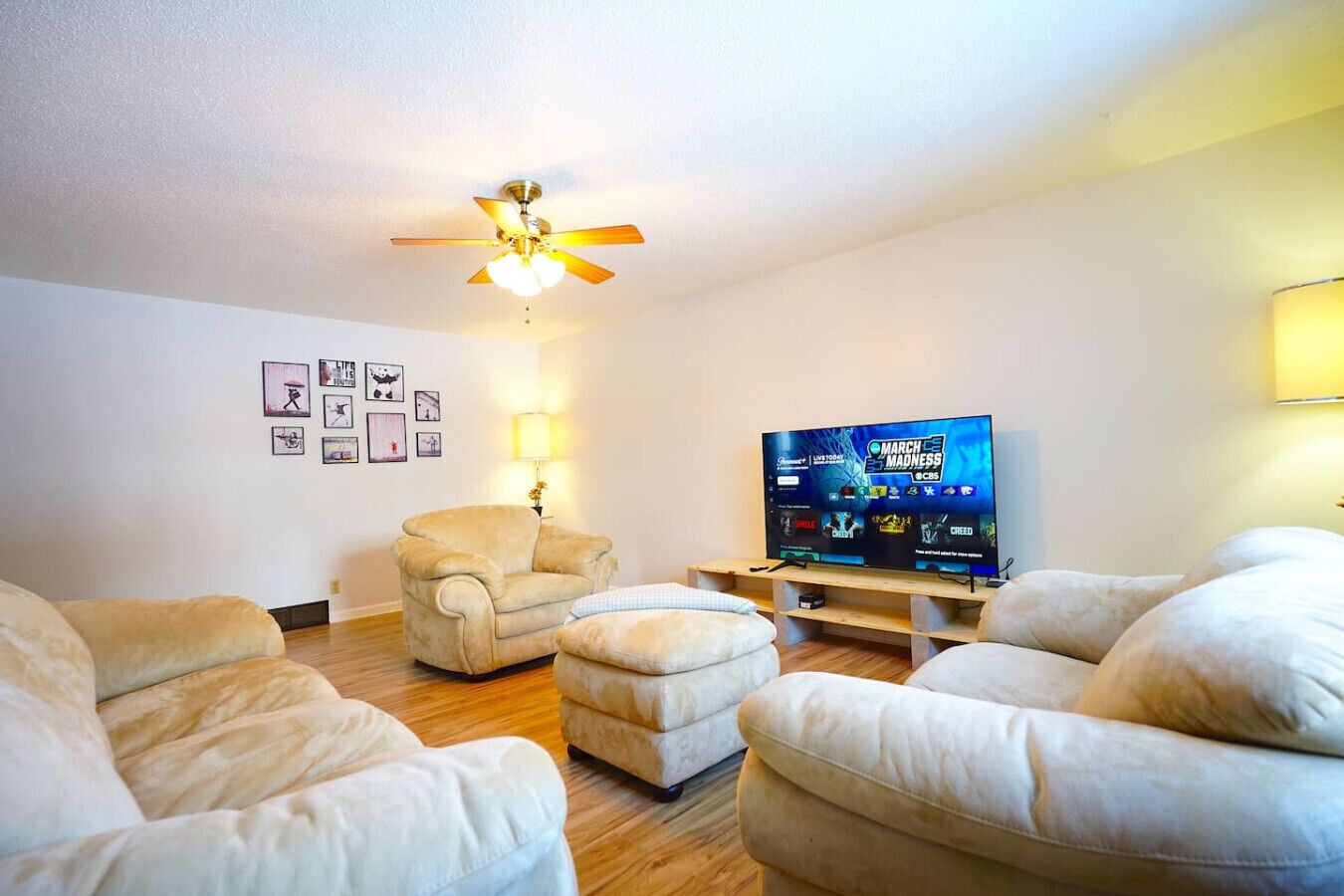 Un salón con ventilador de techo, televisión de pantalla plana y un sillón color beige.