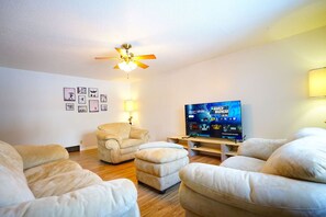 Un salón con ventilador de techo, televisión de pantalla plana y un sillón color beige.