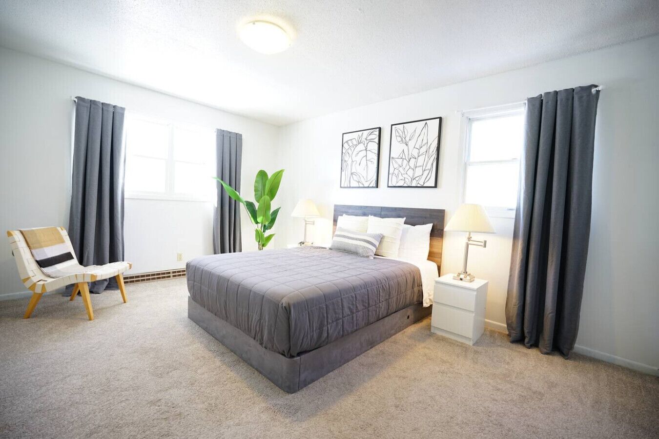 A bedroom with a large bed, two bedside tables with lamps, a chair, and a plant.