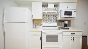 Una cocina compacta con armarios blancos, horno empotrado, microondas y refrigerador.