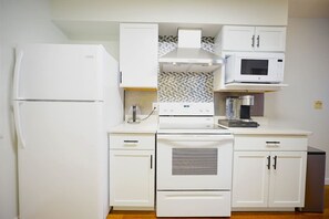 A compact kitchen with white cabinetry, a built-in oven, a microwave, and a refrigerator. - Grand Duplex Blue House (Sioux Falls)