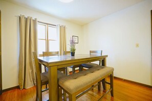 Un comedor con una mesa de madera, dos sillas, un banco y una planta en maceta.
