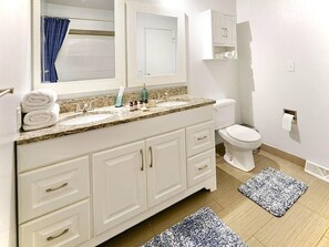 A bathroom with a white vanity, a sink, a mirror, a toilet, and two rugs.