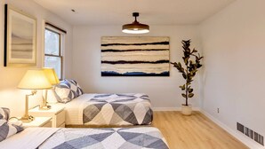 Un dormitorio con cama, mesitas de noche, lámpara, un cuadro abstracto grande y una planta en maceta.