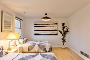 Een slaapkamer met een bed, nachtkastjes, een lamp, een groot abstract schilderij en een potplant.