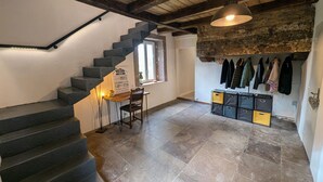 Un escalier avec un plafond en bois et une pancarte sur le mur. On y trouve une table avec une chaise et un porte-manteau avec des vestes.