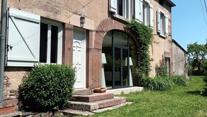 Une maison à deux étages avec une façade en pierre, des volets blancs et une grande fenêtre en arc de cercle.