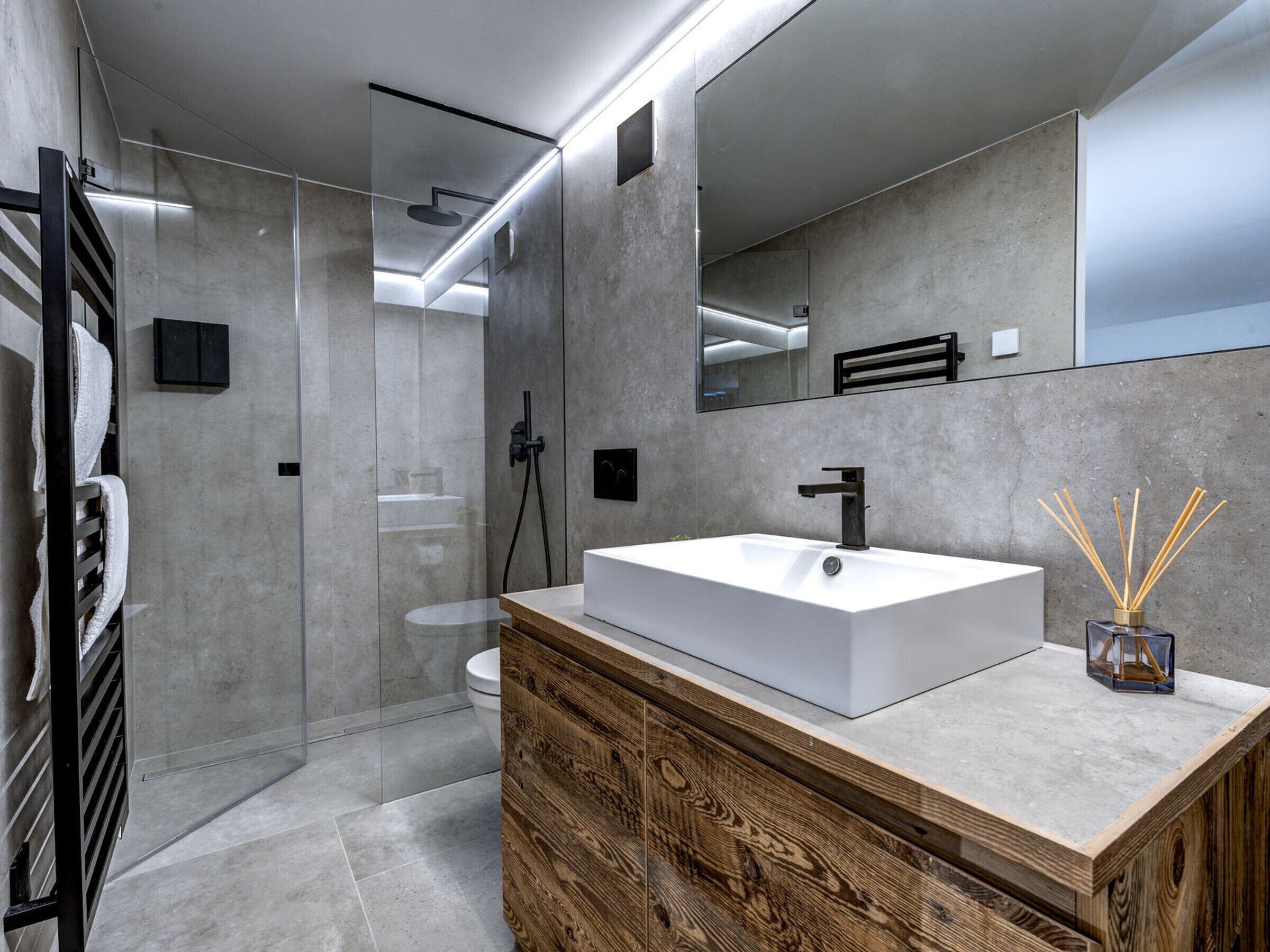 Un baño moderno con un espejo grande, un lavamanos blanco y una ducha con cerramiento de vidrio.