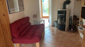 A cozy living room with a red sofa, a fireplace, a small table with a lamp, and a bookshelf.