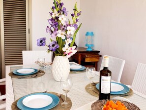 A dining table set with plates, a vase of flowers, a bottle of wine, and a basket of fruit.