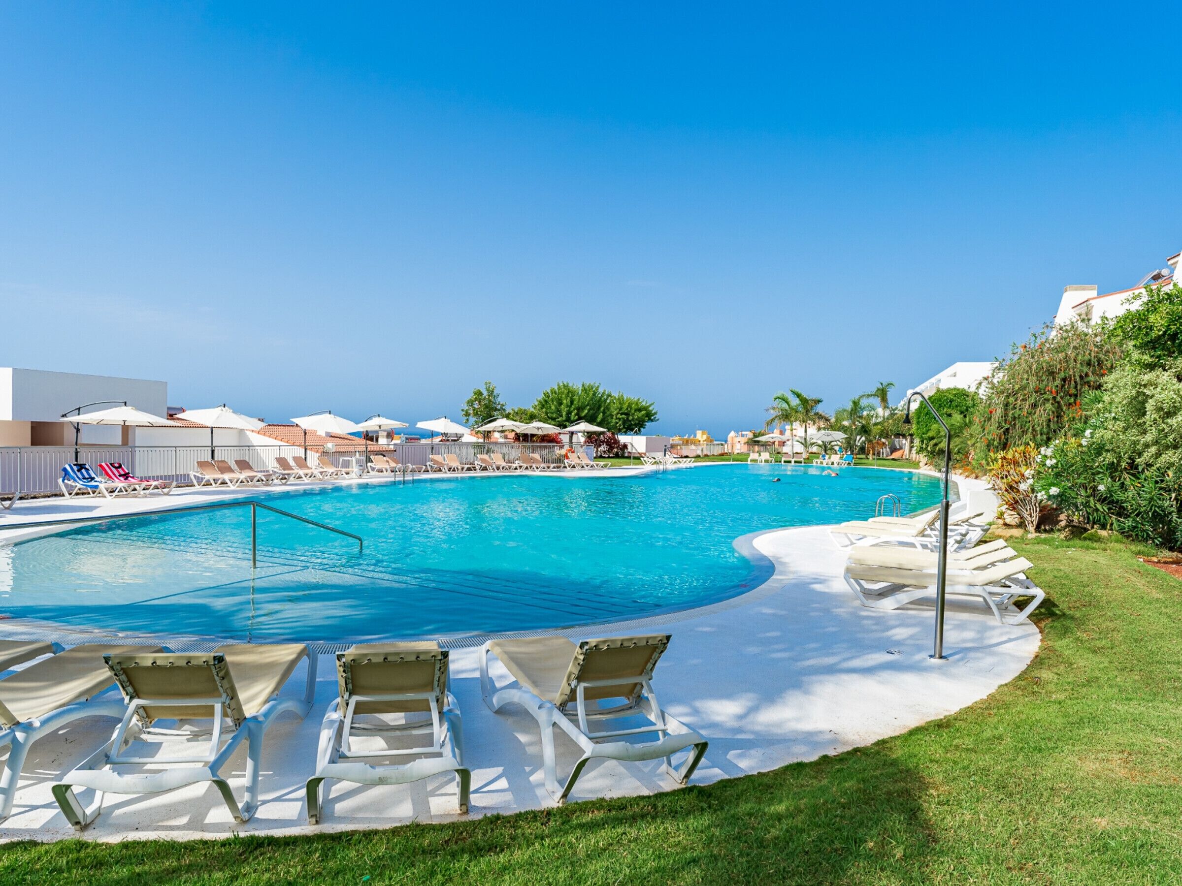 A swimming pool with lounge chairs and umbrellas, surrounded by greenery and buildings.