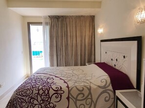 A bedroom with a bed, curtains, a headboard with a floral design, and a wall-mounted light fixture. - Luxury apartment in La Caleta near restaurants (La Caleta)