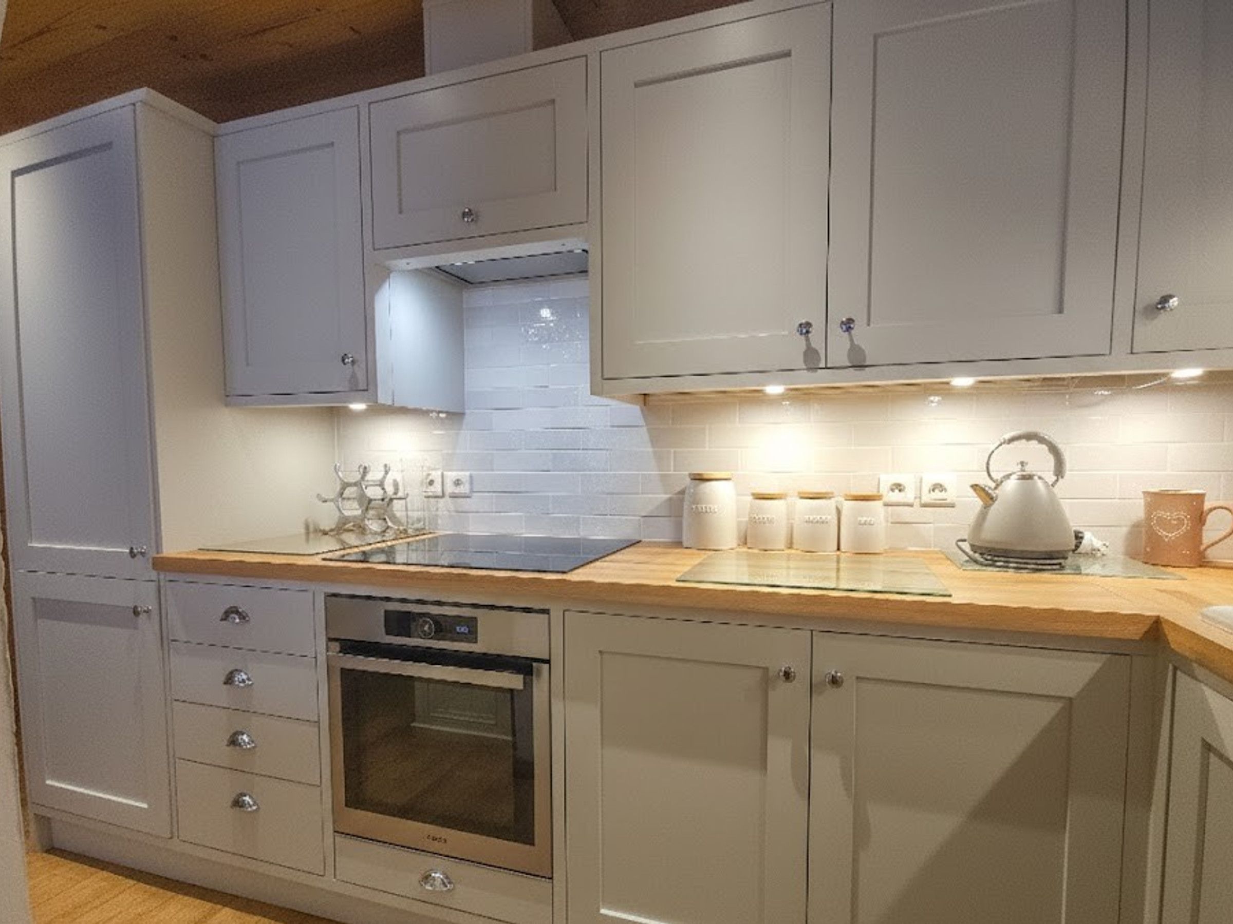A kitchen with grey cabinets, a stainless steel oven, and a kettle on the counter.
