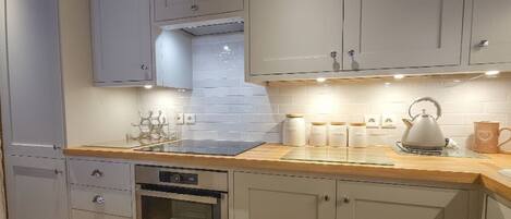 A kitchen with grey cabinets, a stainless steel oven, and a kettle on the counter.