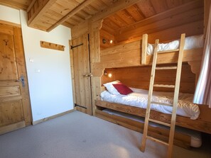 A wooden cabin interior with bunk beds, a ladder, and a door.