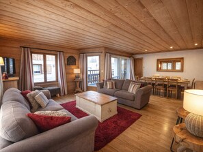 Ein gemütliches Wohnzimmer mit Holzboden, einer Sofagarnitur, einem Esstisch und einem Fernseher.