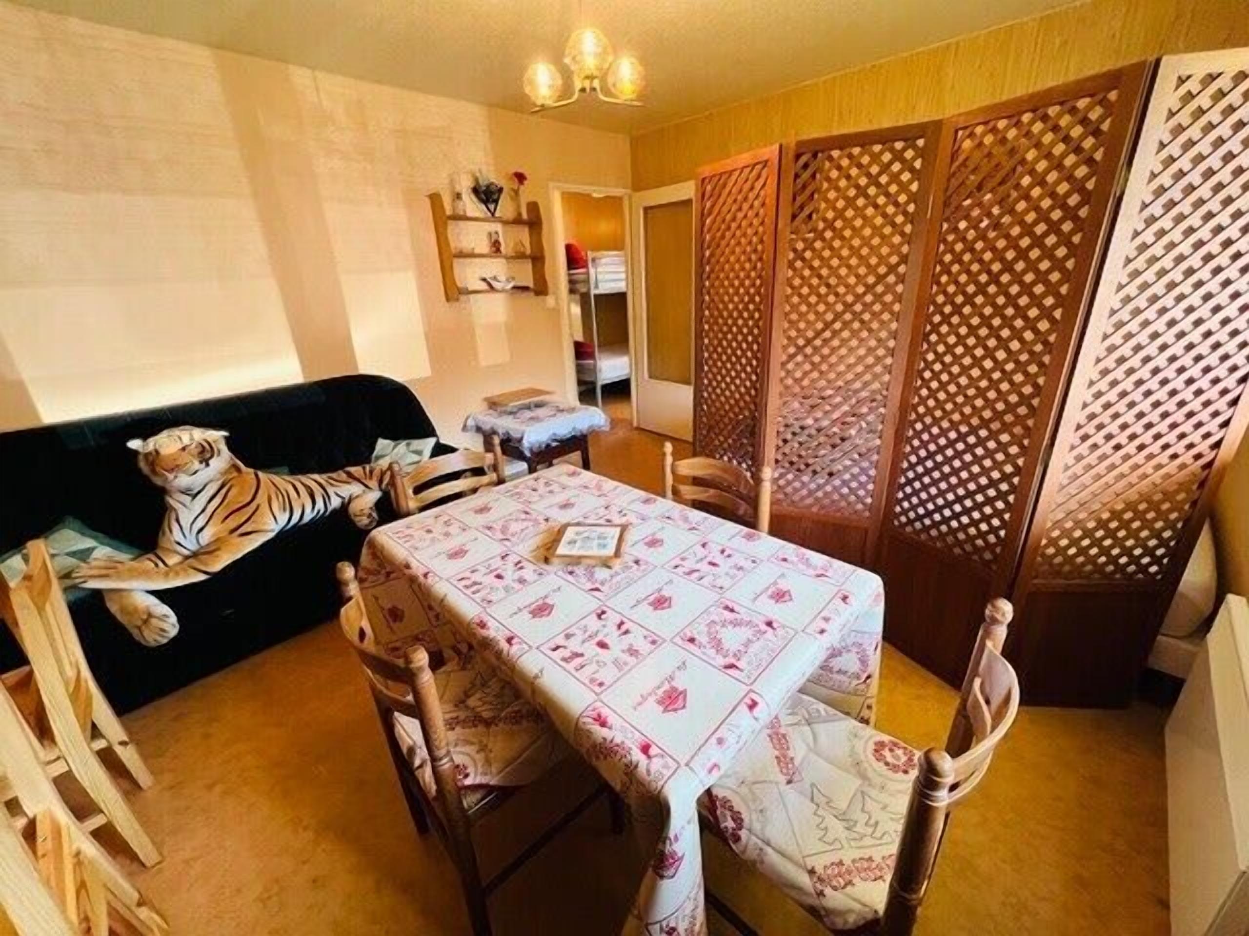 Un coin repas avec une table dressée pour deux personnes, un canapé agrémenté d’un jouet en peluche à l’effigie d’un tigre, et une cloison en bois ornée d’un motif en treillis.