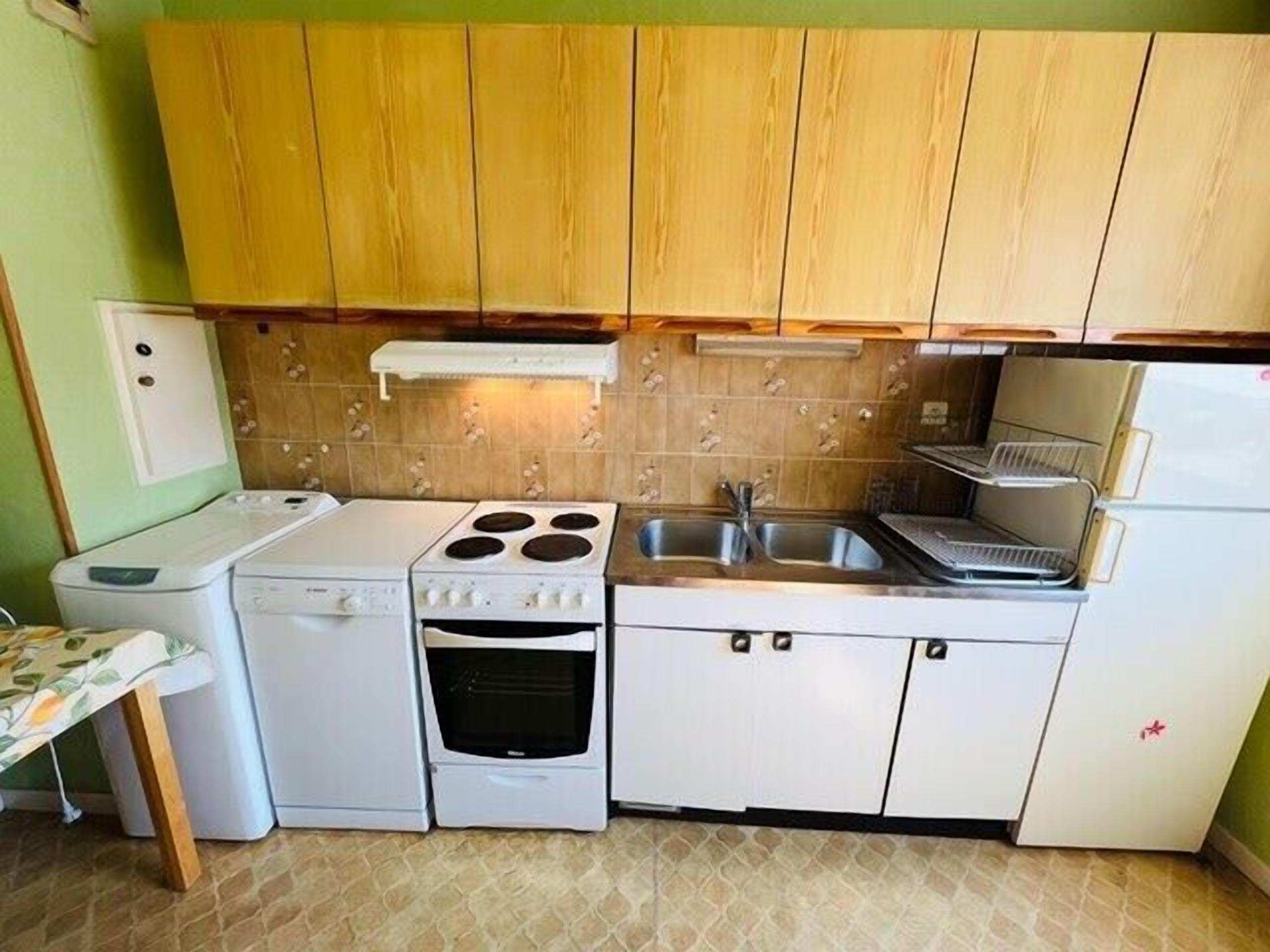 A compact kitchen with a stove, oven, sink, and a small refrigerator.