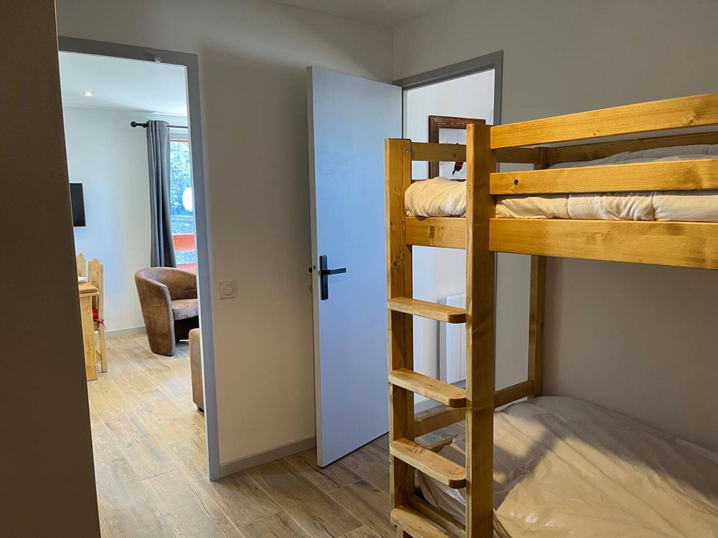 A bunk bed in a room with a door leading to another room.