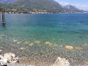 Un lac aux eaux limpides, bordé d’une rive rocheuse, avec une ville qui se devine au loin.