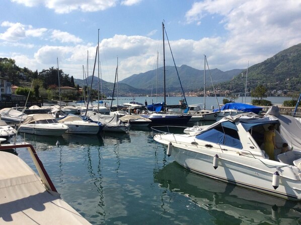 A marina with multiple boats docked, calm water, and a mountainous backdrop.