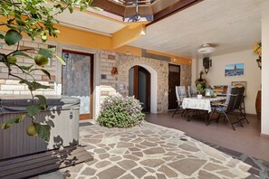 An outdoor patio with a stone floor, a hot tub, a small bush, a dining table with chairs, and a stone wall.
