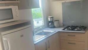 A compact kitchen with a microwave, stove, sink, and cabinets. - Mobile home in Argences en Aubrac - 6 pax, Terrace (Argences-en-Aubrac)