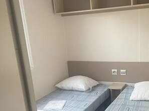 A single room with two beds, each with a pillow and a blanket. There are two bedside tables, one on each bed. The walls are plain and there is a window on the left side of the room. - Mobile home in Argences en Aubrac - 6 pax, Terrace (Argences-en-Aubrac)