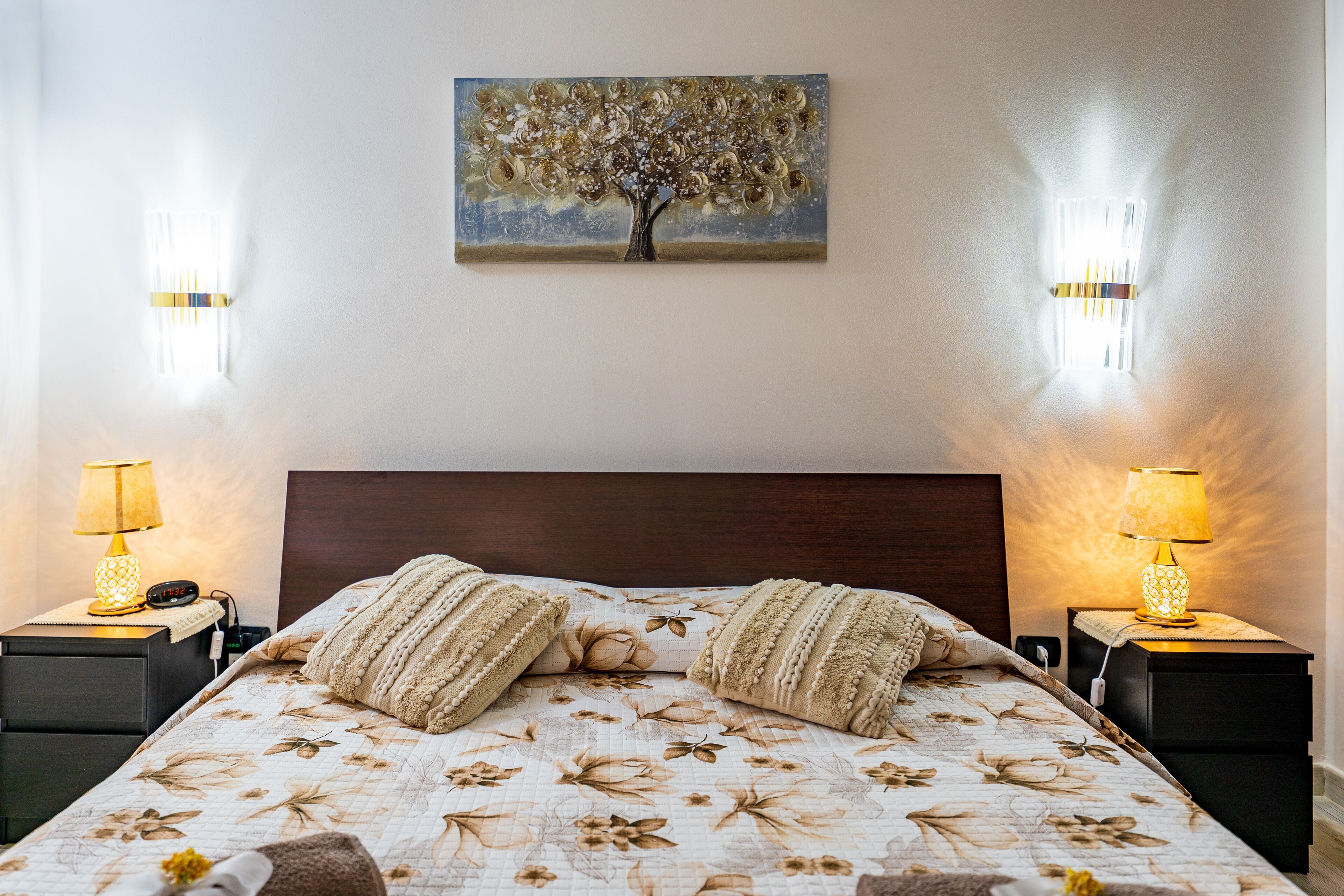 A bedroom with a bed, two bedside tables, a nightstand, a lamp, and a painting on the wall.