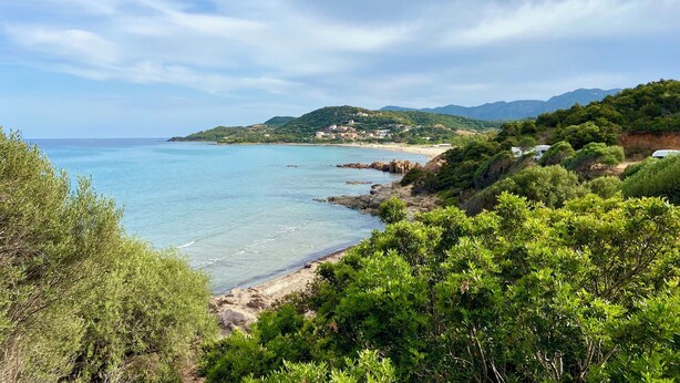 Un paisaje costero con una vista despejada del mar, colinas verdes y una carretera que lleva a una zona de playa.