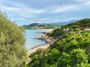 A coastal landscape with a beach, rocky shoreline, and lush greenery.
