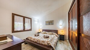Un dormitorio con cama, mesitas de noche, escritorio y ventana con cortinas.