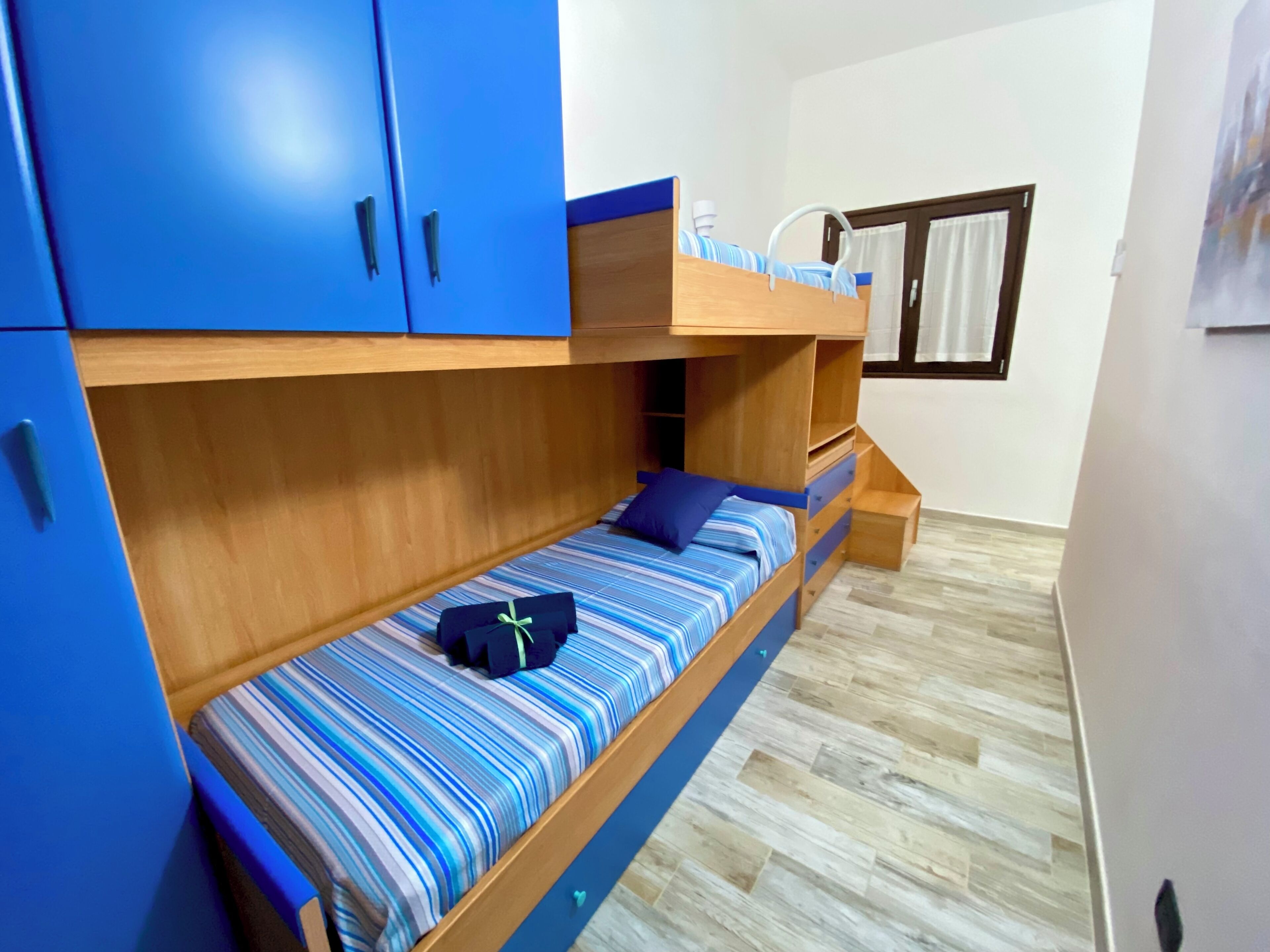 Une chambre avec un lit superposé, une tête de lit en bois, un petit bureau et une fenêtre avec des rideaux.