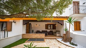 Un patio con un camino de piedra, una zona de estar con mobiliario exterior y un árbol que da sombra.