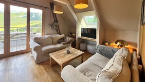 Ein geräumiges Schlafzimmer im Loft-Stil mit einem großen Dachfenster, einer gemütlichen Sitzecke mit Sofa und Couchtisch sowie einem Fernseher auf einem Regal.